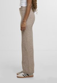 Světlé béžové kalhoty s širokými nohavicemi vyrobené z jemné, strukturované látky s vroubkovaným pasem. Vytvořené v kombinaci s bílými teniskami s černými a béžovými akcenty.