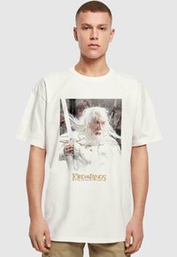 Witte katoenen t-shirt met een afbeelding van een oude man met lang wit haar en een zwaard, met de tekst "The Lord of the Rings: The Return of the King".