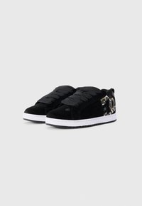 Svarte semskede sneakers med en hvit gummisåle, med teksturerte svarte snøringer og et mønstret side design i brunt og svart.