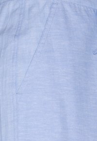 Svetle modrá látka zblízka ukazující hladký, texturovaný povrch s diagonálním švem a detaily kapsy.