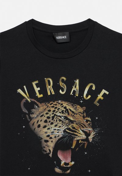 Tricou negru cu guler rotund, cu un grafic al capului unui leopard care răcnește și text mare auriu „VERSACE" deasupra capului animalului.