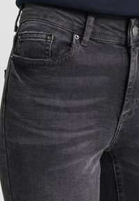 Jeans de mezclilla negra con un corte ajustado, que cuentan con cinco bolsillos, cierre de botón y una sutil textura desgastada a lo largo de la tela.