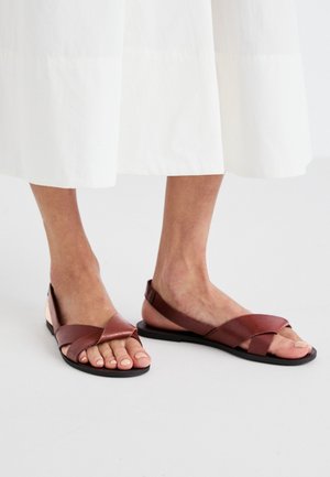 Brune lædersandaler med krydsremdesign, flad sål og åben hæl. Tekstureret finish og minimalistisk stil.