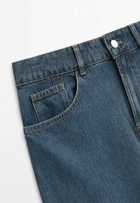 Gros plan de la taille d'un jean en denim bleu avec poche avant, petite poche à monnaie, passants de ceinture et fermeture par bouton métal sur fond blanc.