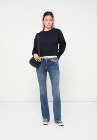 Marinblå kortärmad tröja med långa ärmar, matchad med blå raka jeans. En svart handväska och svart-vita sneakers fulländar looken.