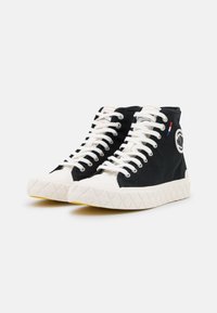 Baskets montantes noires avec des lacets blancs, semelle en caoutchouc présentant un motif texturé, détail de logo circulaire et accents de couture contrastants.