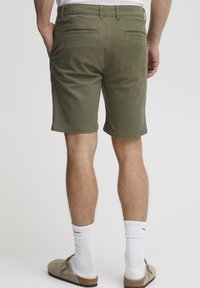 Grønne bomullsshorts med flat front, to baklommer og rett snitt. Brukt med hvite sokker og lyse slip-on sko.