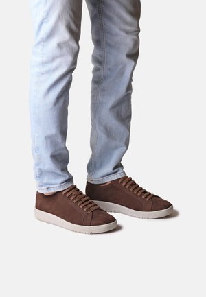 Hnědé semišové vysoké tenisky s béžovými gumovými podrážkami, se zaoblenými tkaničkami a hladkým povrchem. Nosené s světle modrými džínami.