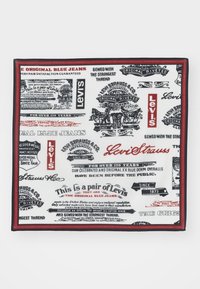 Levi's-merket stoff med svart og rød tekst på hvit bakgrunn, som viser vintage logoer og annonser relatert til blå jeans.