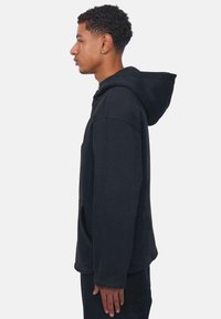 Schwarze Kapuzenpullover mit lässigem Schnitt, großer Kapuze und vorderen Taschen. Verfügt über lange Ärmel und einen weichen Stoff. Seitliche Ansicht dargestellt.