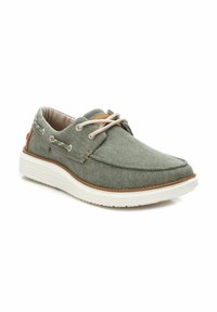 Zapatilla de lona verde con superficie texturizada, cordones beige, suela de goma blanca y detalles en marrón en el talón.