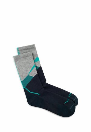 Calcetines a la altura de la tripulación en gris y negro con patrones geométricos de montañas en azul verdoso y detalles en azul verdoso en los dedos y puños, colocados planos sobre un fondo blanco.