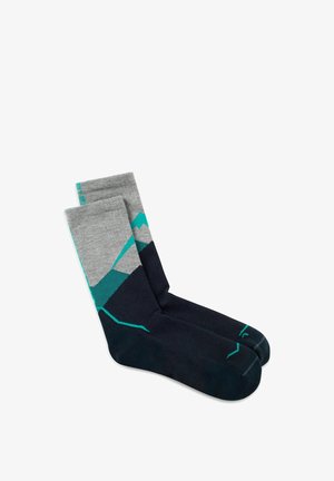 Calcetines a la altura de la tripulación en gris y negro con patrones geométricos de montañas en azul verdoso y detalles en azul verdoso en los dedos y puños, colocados planos sobre un fondo blanco.