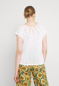 Top blanco de manga corta con un diseño de encaje texturizado en el escote trasero. Combinado con pantalones de estampado floral que presentan girasoles.