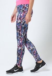 Leggings multicolori con un motivo astratto blu, rosa e nero, dal taglio slim e con una striscia laterale rosa. Abbinati a scarpe da ginnastica nere.