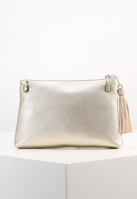 Metallisk guldpose med en tekstureret overflade, lynlåslukning og en beige frynseaccent på den ene side. Enkel, rektangulær design.