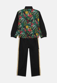 Ζακέτα με λουλουδάτο μοτίβο, μαύρα μανίκια και γιακά, συνδυασμένη με μαύρο παντελόνι που έχει χρυσές ρίγες στο πλάι. Υλικά: μείγμα υφασμάτων.