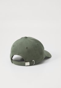 Olijfgroene katoenen baseballpet met een gebogen rand, verstelbare band en metalen accent aan de achterkant. Getextureerde stof met stikseldetails.