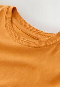 Oranž puuvillane kangas koos ribaga ümmarguse kaelusega disainiga. Tekstuur tundub sile ja kerge venivusega, näidates lihtsat ja puhta esteetikat.
