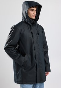 Musta vedenpitävä takki, jossa on huppu, nepparit ja säädettävät nyörit. Siinä on sivutaskut ja sileä, matta viimeistely.