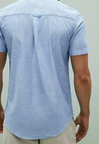 Koszula z krótkim rękawem w jasnoniebieskim kolorze, wykonana z miękkiej tkaniny o gładkiej fakturze, z zaokrąglonym dołem i centralnym zakładką na plecach.