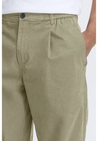 Pantalon kaki en coton à texture lisse, avec une ceinture élastique, des poches latérales et une fermeture à bouton unique.