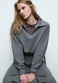 Grå sweatshirt med bred krave, lagd over en stribet bordeaux og hvid skjorte. Blød tekstur, afslappet pasform og ribbet manchetter.