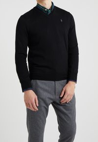 Black v-neck sweater made of a fine knit material, layered over a green and blue checkered shirt with a rounded collar.