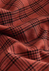 Punane ja must kontrollmuster, millel on tekstureeritud pind, näidates ristuvaid jooni ja erineva paksusega mustrit, rippuv ja voolav.