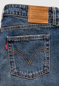 Jean en denim bleu avec une poche arrière affichant la languette rouge Levi's et une étiquette en cuir marron Levi Strauss & Co. au-dessus de la ceinture.