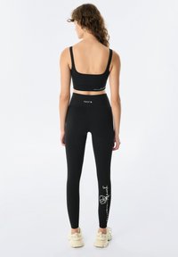 Czarny zestaw aktywnej odzieży składający się z dopasowanej bluzki crop i legginsów z wysokim stanem. Legginsy mają biały graficzny wzór z boku.