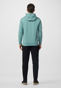 Sudadera azul claro con bolsillo tipo canguro, puños acanalados y dobladillo. Combinada con pantalones deportivos negros y zapatillas negras.