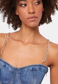 Top in denim con design a spalline; presenta spalline in catena dorata, scollatura strutturata e cuciture visibili. Tessuto blu con leggera texture sbiadita.