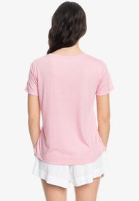 Roze T-shirt met korte mouwen en een ronde halslijn, gemaakt van lichtgewicht materiaal en met een relaxte pasvorm. G gedragen met witte, gestructureerde shorts.