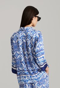 Blauw en wit gestreepte blouse met ingewikkelde bloemenpatronen, zachte stof, relaxte pasvorm, driekwartmouwen en een effen blauwe rand.