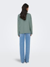Pull vert clair oversize avec épaules tombantes, associé à un jean large taille haute bleu clair. Coupe décontractée et texture lisse.