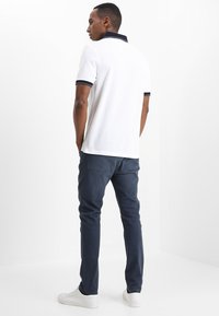 Camisola polo branca com colarinho e punhos em azul marinho, combinada com calças azul marinho e ténis brancos. Ajuste casual e textura suave de algodão.