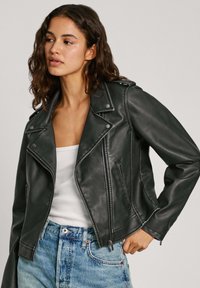 Zwarte leren motorjack met een asymmetrische ritssluiting, epauletten en zijzakken, gecombineerd met een witte tanktop en blauwe jeans.