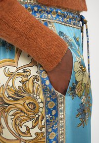 Fustă din mătase cu un fundal albastru, decorată cu modele florale intricate și motive ornate aurii; include o buzunar lateral și un talie ajustată.