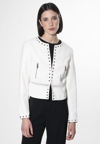 Giacca bianca cropped in faux leather, dotata di zip argentate, dettagli di borchie attorno al collo e un intreccio in vita.