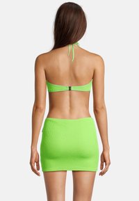 Bikini deux pièces vert néon avec une finition texturée ; haut à col halter et mini-jupe assortie, doté d'une fermeture à clip à l'arrière.