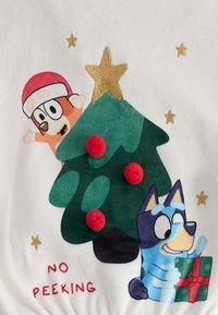 Weißer Stoff mit einem Weihnachtsbaum, rot-weißen Pompons, einem goldenen Stern und Cartoonfiguren, mit dem Aufdruck "Nicht Spicken" in Rot.