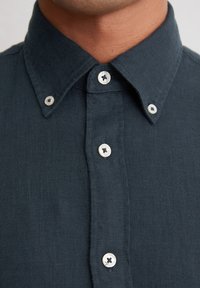 Donkerblauwe linnen shirt met een klassieke kraag, verfraaid met witte knoopaccenten en zichtbare stikdetails langs de knoopsluiting.