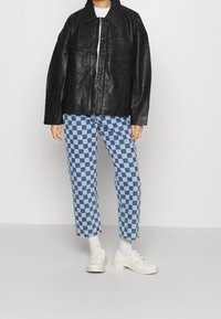 Sort læder oversized jakke med to forlommer, parret med bukser i blåt ternet mønster og hvide loafers.