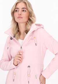 Világos rózsaszín, kapucnis dzseki puha, sima anyagból. Fényes zsinórokkal és fa gyöngyökkel rendelkezik, cipzáras záródása és két elülső zsebe van.