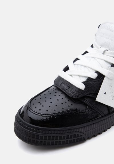 Ασπρόμαυρο αθλητικό παπούτσι με διάτρητη μύτη, λευκά κορδόνια, υφασμένα δερμάτινα πάνελ και χοντρή ραβδωτή σόλα σε λευκό φόντο.