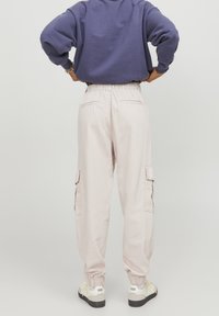 Světlé růžové cargo kalhoty s elastickým pasem, manžetami na kotnících a bočními kapsami. Materiál vypadá měkký a texturovaný, vhodný pro každodenní nošení.