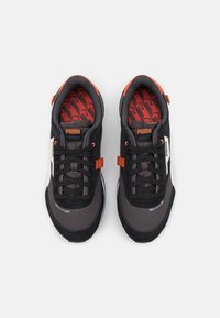 Scarpe sportive nere con tomaia in rete grigia scura e accenti in suede neri. Presentano dettagli arancioni, logo e una soletta stampata con branding.