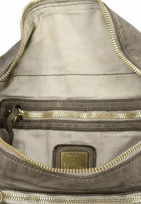 Intérieur d'un sac à main en daim marron, avec une fermeture éclair dorée, une doublure en tissu et une étiquette de logo portant la mention "CAMPOMAGGI 25.02.1961" en relief.