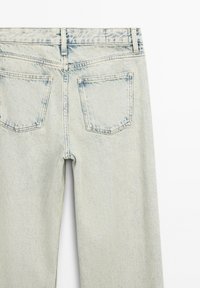 Jean en denim bleu clair délavé vu de dos avec deux poches, des passants pour ceinture et des coutures visibles.